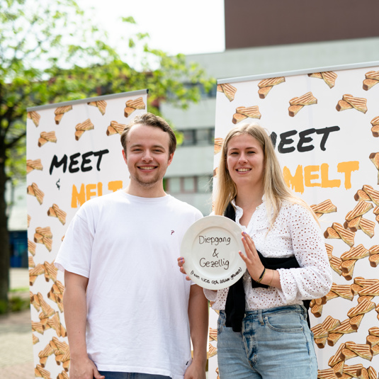 Foto van twee studenten voor banieren met 'Meet & Melt' erop